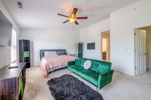 A bedroom with a bed, a green sofa, a ceiling fan, and a door leading to another room. - Home Gym & Pool Access! North Raleigh Retreat (Raleigh)