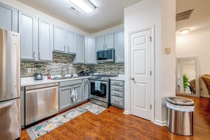 A modern kitchen with grey cabinets, a stainless steel refrigerator, a microwave, and a stove. - Home Gym & Pool Access! North Raleigh Retreat (Raleigh)