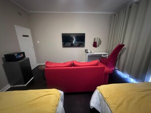 Een hotelkamer met een rode bank, een wit bureau, een televisietoestel en een bed met een gele spreidek.