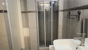 Casa de banho com lavatório branco, cabine de duche em vidro e porta branca.
