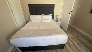 A neatly made bed with a black headboard, a bedside table with a lamp, and a wooden floor. - Room-comfortable Guest Room in Ekurhulen (Germiston)