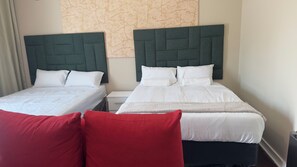 A hotel room with two beds, each with a green upholstered headboard, white bedding, and a red accent pillow. - Room-comfortable Guest Room in Ekurhulen (Germiston)