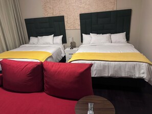 Een hotelkamer met twee bedden, elk met een donker hoofdeinde en witte beddengoed. Op de bedden liggen rode en gele sierkussens.