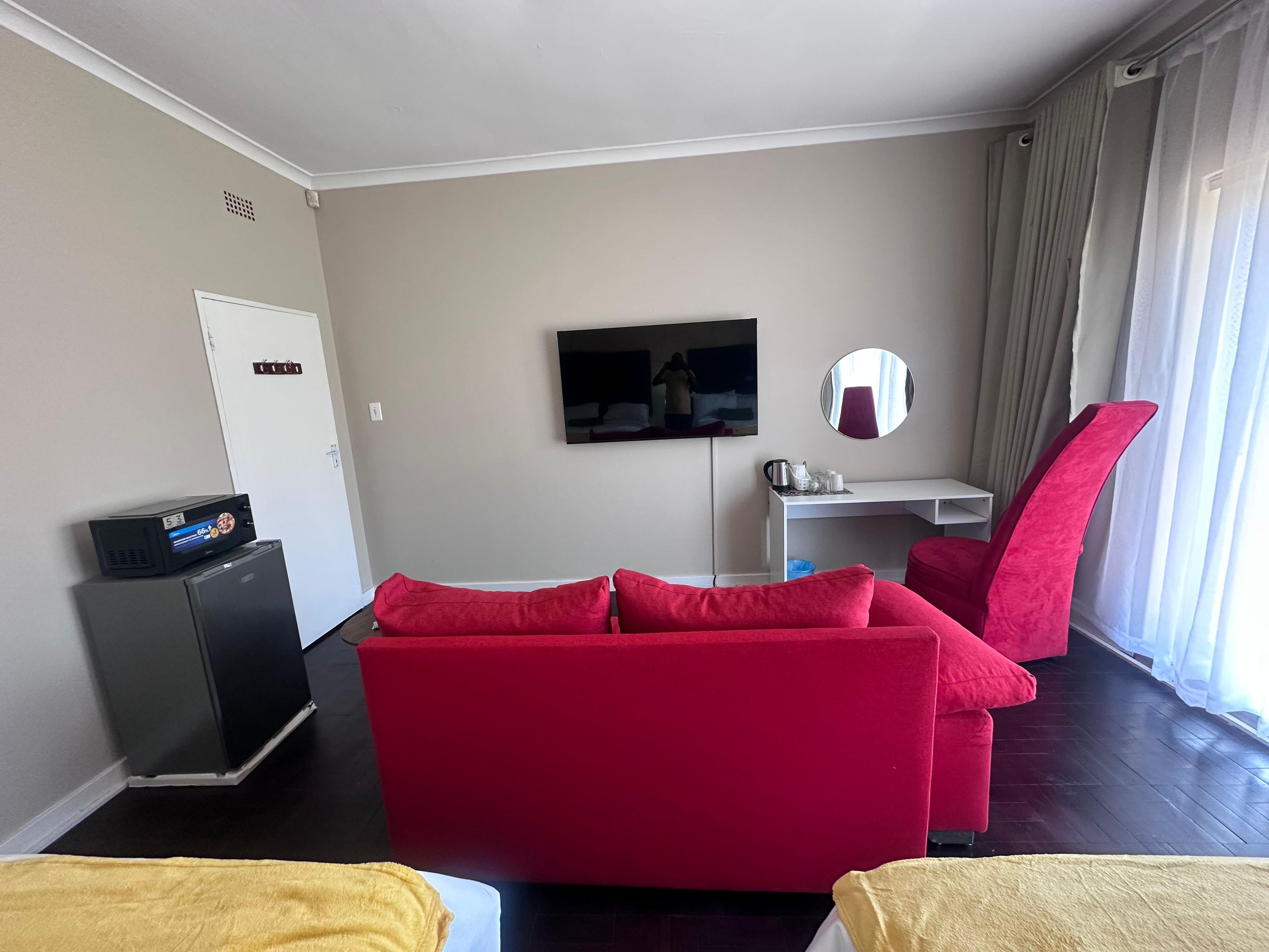 A hotel room with a red sofa, a small desk, a television, and a mirror.