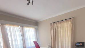 Quarto de hotel com uma cama grande, um sofá vermelho, uma escrivaninha com chaleira e televisão.