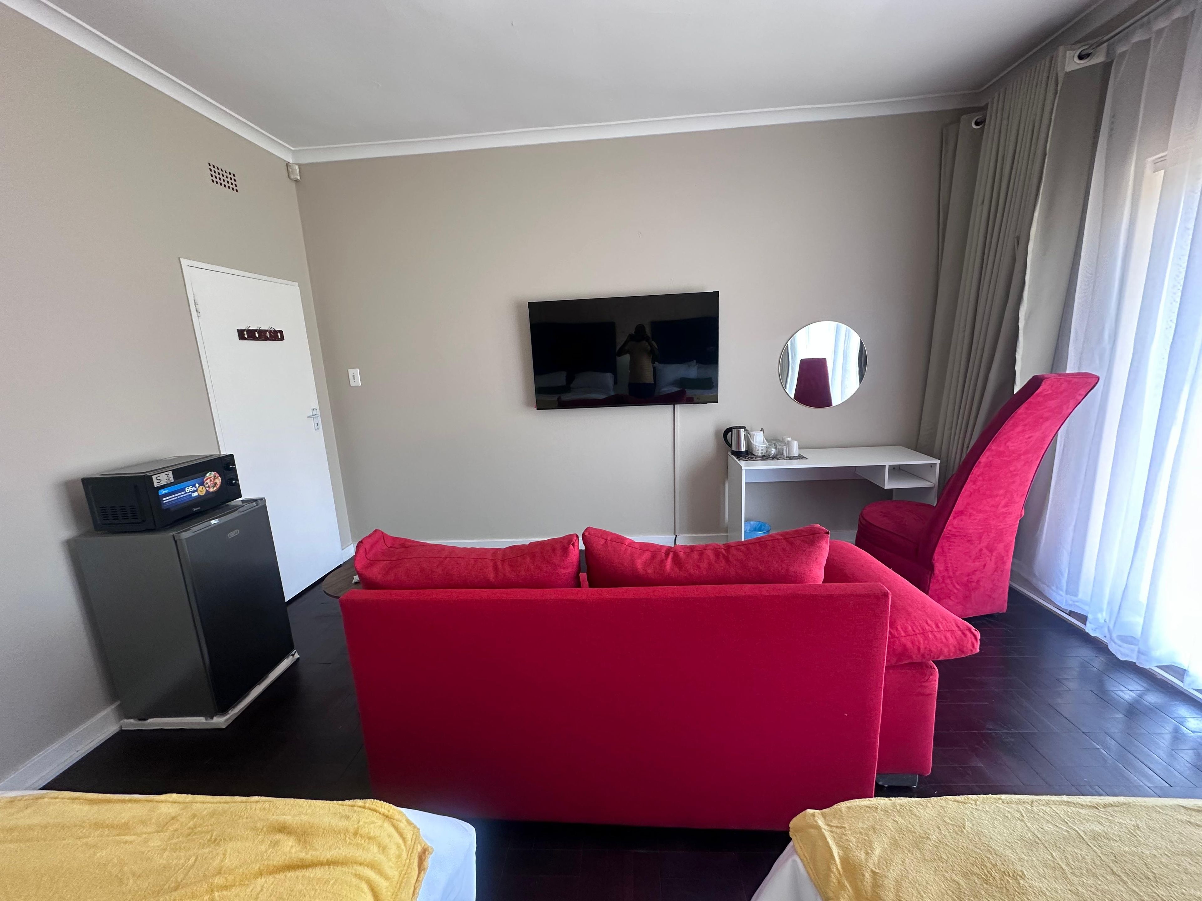 A hotel room with a red sofa, a small desk, a television, and a mirror.