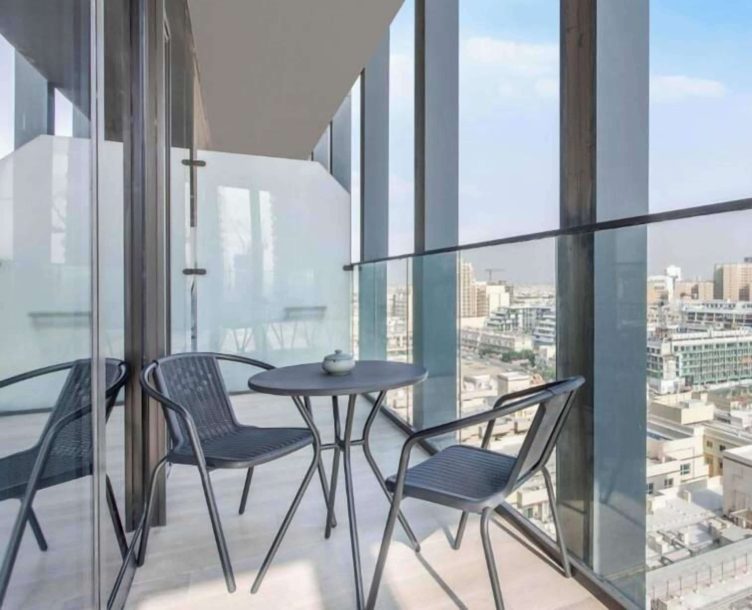 Ein Balkon mit Glasgeländer, zwei Stühle, ein kleiner Tisch und Blick auf die Stadt.