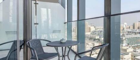 A balcony with a glass railing, two chairs, a small table, and a city view.