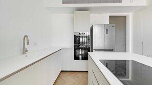 A modern kitchen with white cabinetry, a stainless steel refrigerator, and a built-in oven. - Spacious 3BR Apartment in Neve Tzedek by BARNES Israel (Tel Aviv-Yafo)