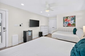 Ein Schlafzimmer mit Bett, Fernseher, Kommode, Schreibtisch, Deckenventilator und einer Tür.