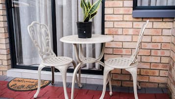 A patio with two white metal chairs and a small round table, a potted plant, and a doormat.