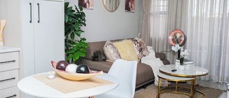 A modern living room with a dining area, a sofa, a coffee table, and a small side table with a fan.