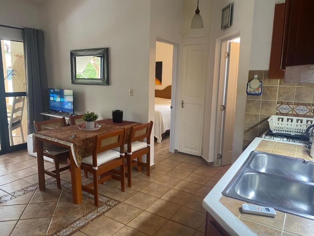 Une cuisine équipée d’un évier, une table à manger avec des chaises, un téléviseur et une porte donnant sur une autre pièce.