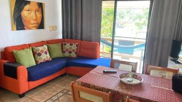 Sala de estar com sofá, mesa de jantar e vista para varanda.