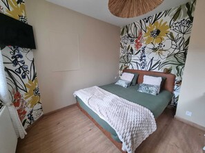 Ein Schlafzimmer mit einem Bett, einem an der Wand montierten Fernseher und floralem Wandpapier.