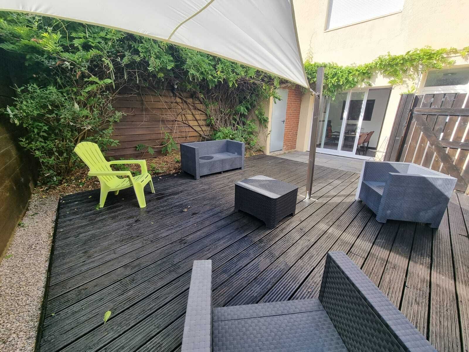 A wooden deck with outdoor furniture, including a bright yellow chair and two grey sofas, under a white canopy.
