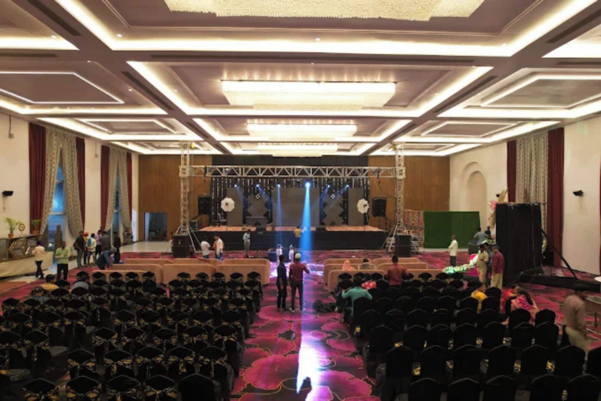 Un amplio salón con asientos escalonados, un escenario con iluminación y una pantalla verde.