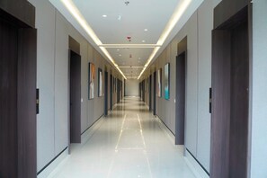 A long, narrow hallway with doors on both sides, recessed lighting, and framed artwork on the walls. - Prithvi Palace (Durg)