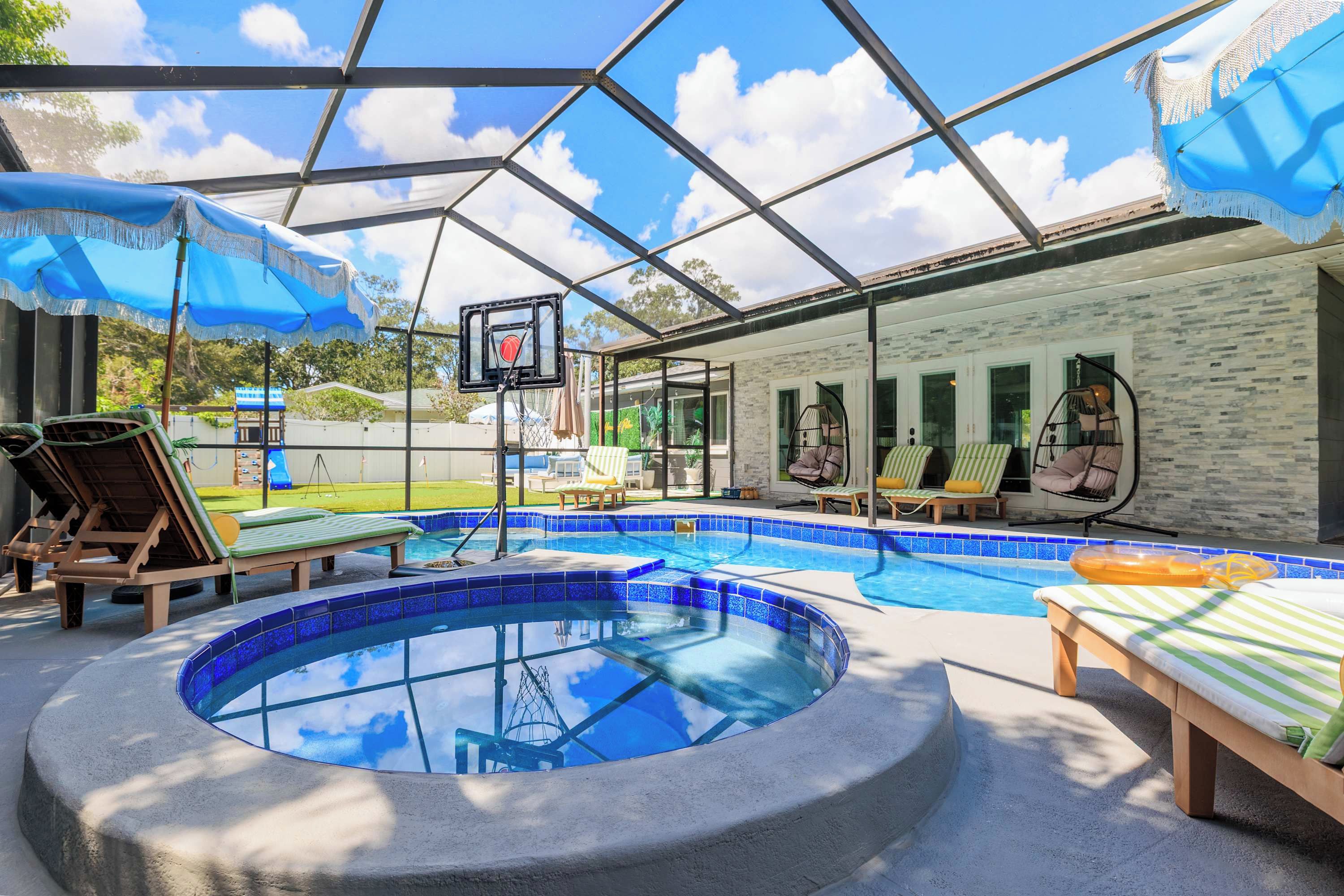 Una piscina con jacuzzi, sillas de descanso y un aro de baloncesto.