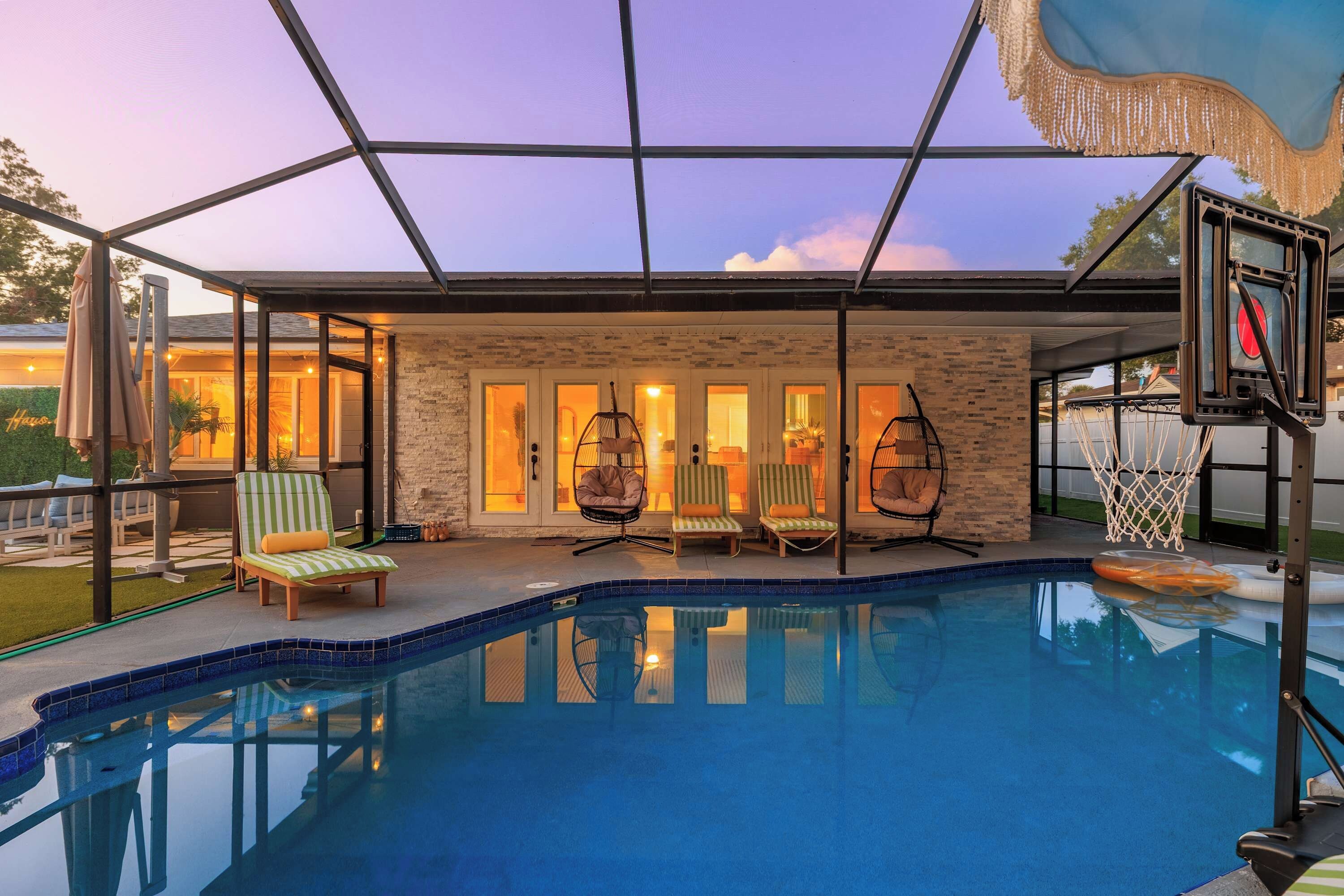 A swimming pool with a glass enclosure, surrounded by lounge chairs and a basketball hoop.