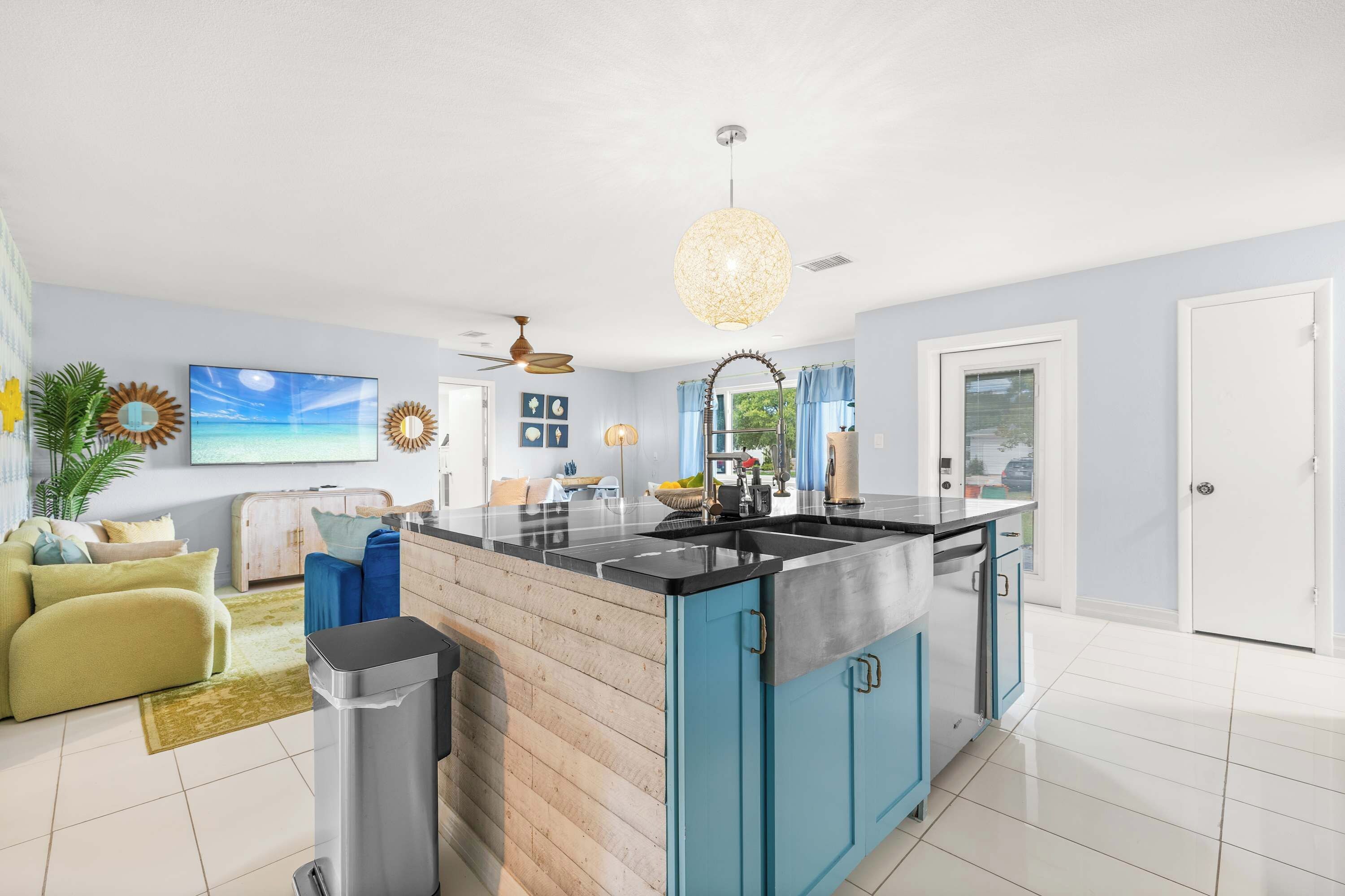 A modern kitchen with a central island, a ceiling fan, and a large window with curtains.