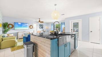 A modern kitchen with a central island, a ceiling fan, and a large window with curtains.