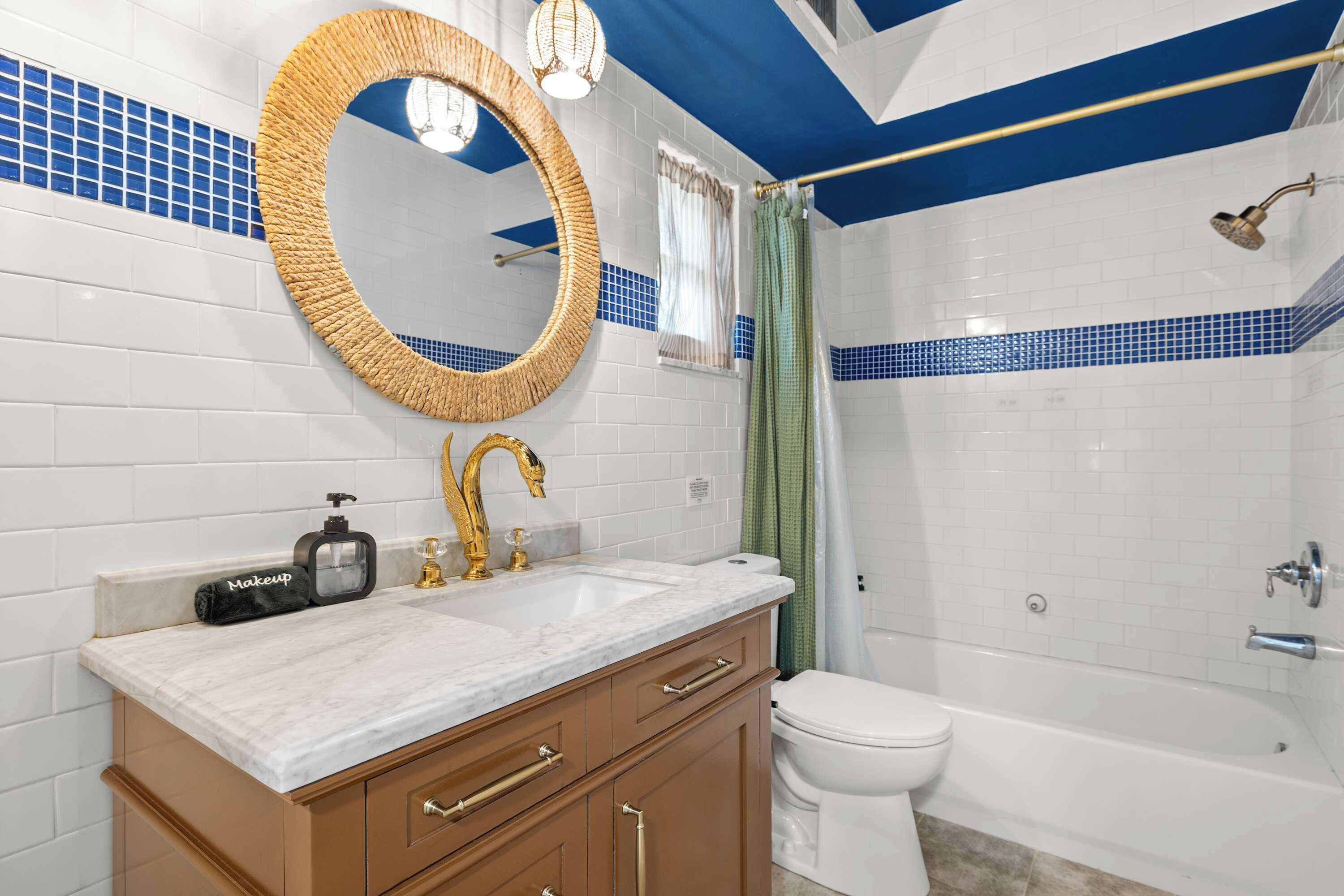Une salle de bain avec un mur recouvert de carreaux blancs, un miroir rond, un robinet doré, des toilettes blanches et une baignoire.