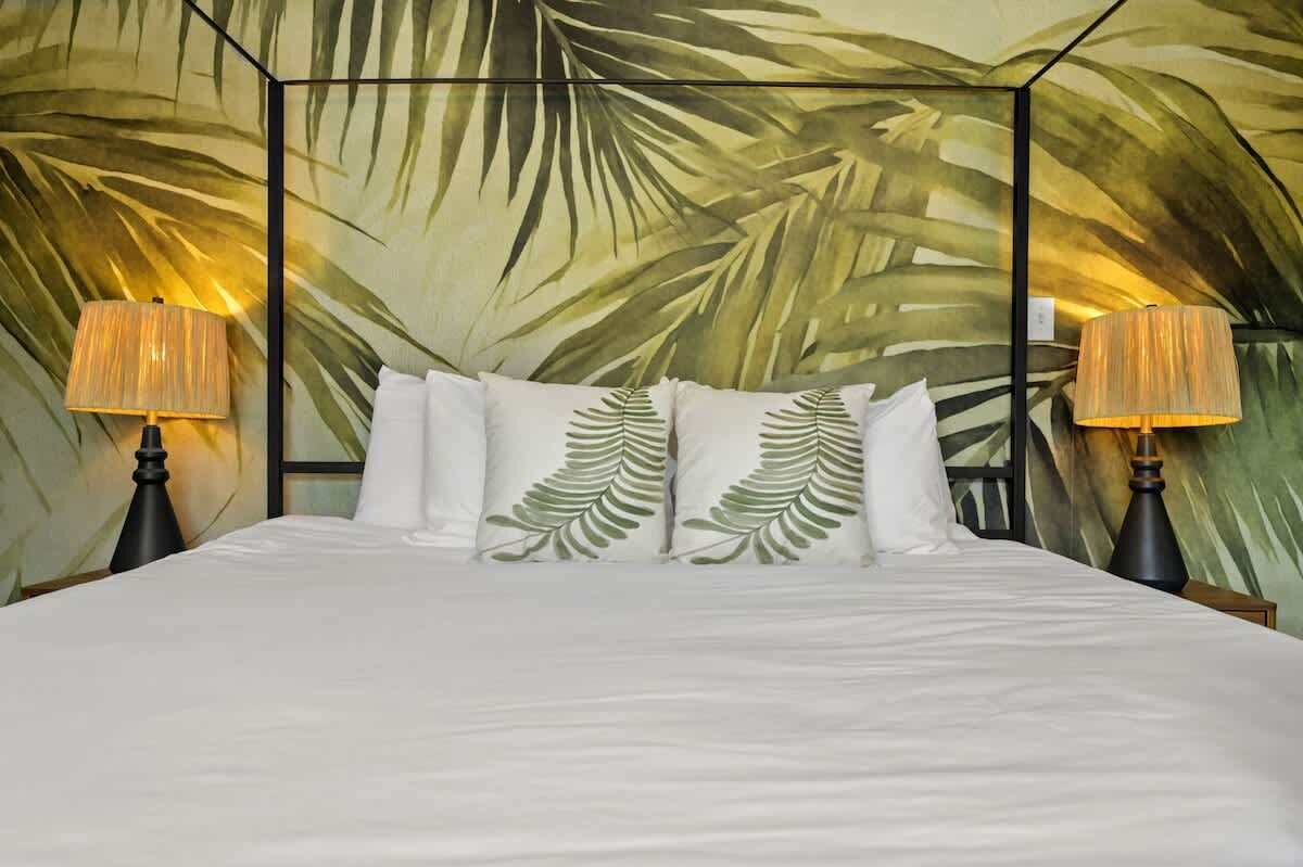 A bed with white bedding and decorative pillows, flanked by two lamps with lampshades.