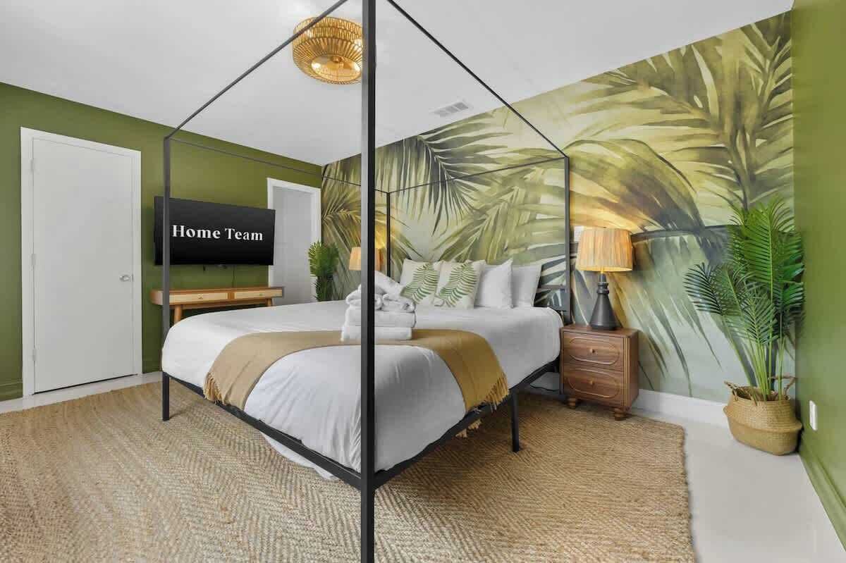 Een slaapkamer met een hemelbed, een televisie, een muurschildering en een nachtkastje met een lamp.