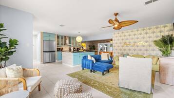 Una sala moderna con un sofá azul, un sillón blanco y un comedor con una mesa azul.