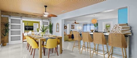 A modern dining area with a high ceiling, a dining table set for six, and wicker bar stools.