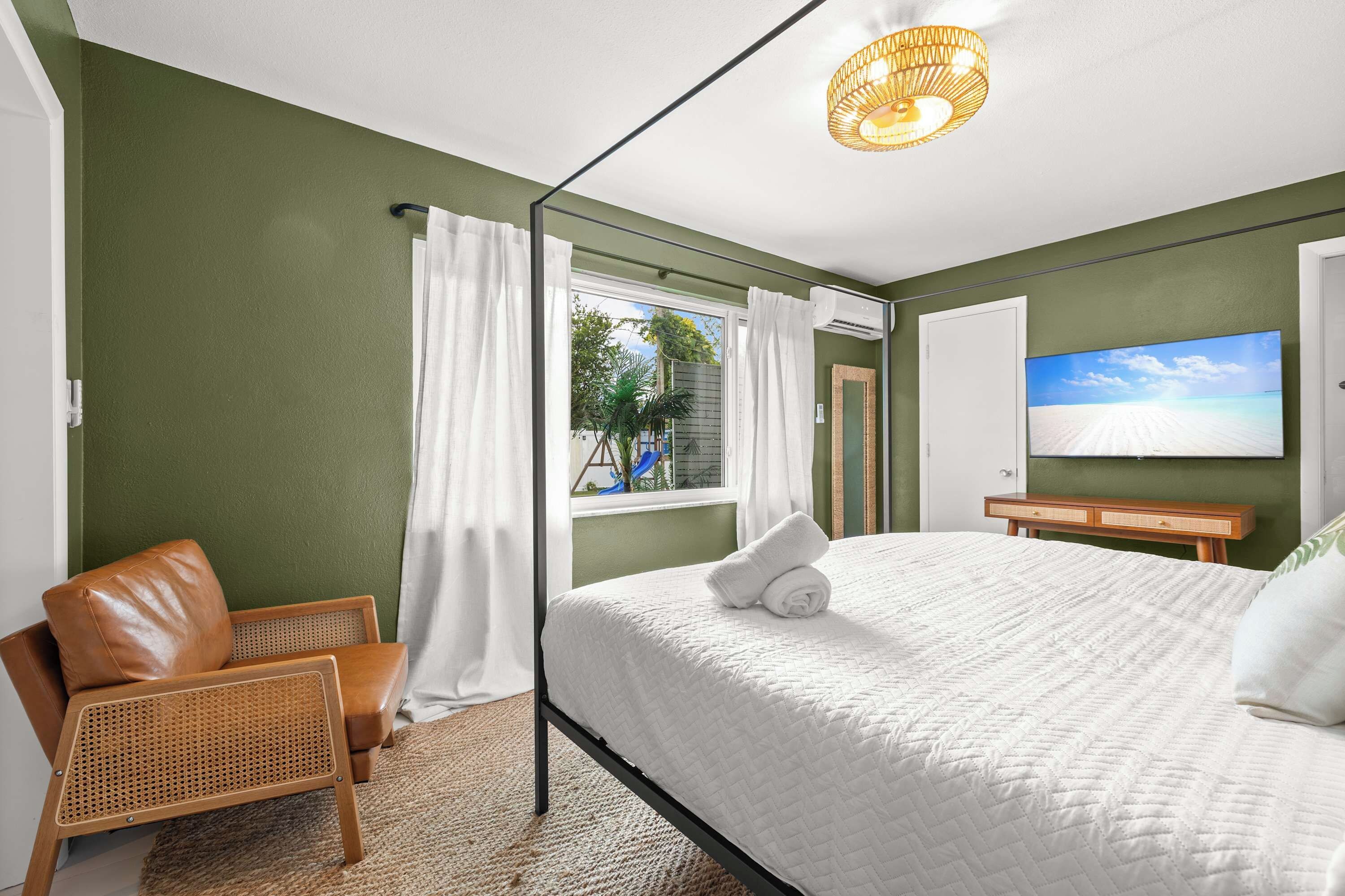 A bedroom with a bed, a chair, a television, and a window with curtains.