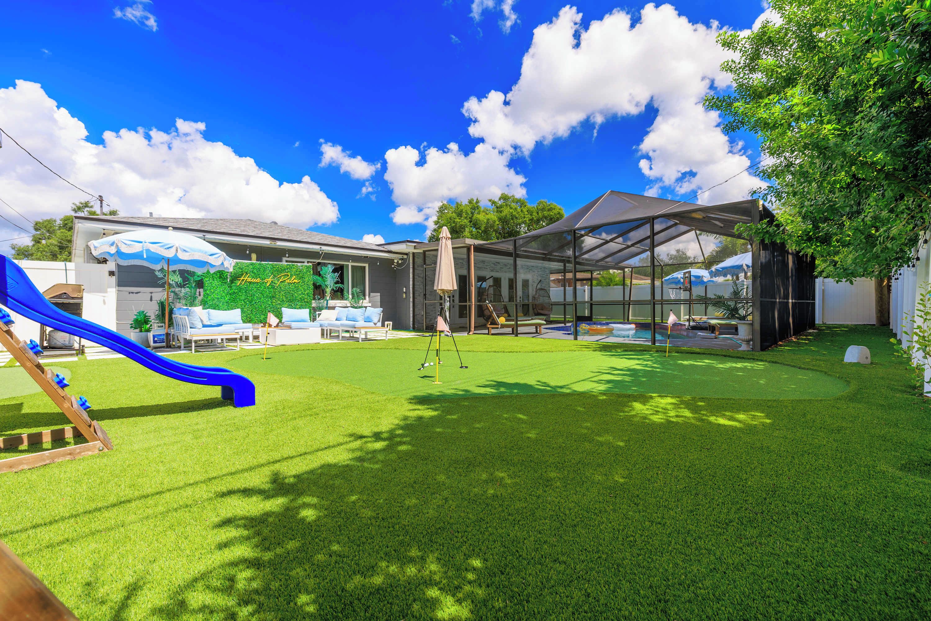 A backyard with a slide, a covered seating area, and a house with a green wall.