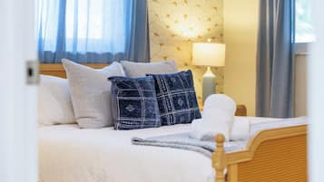 A neatly made bed with white bedding and a few pillows, a bedside lamp, and a window with curtains.
