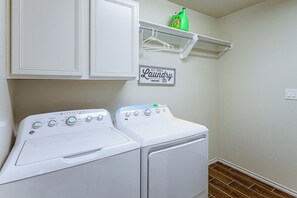 Una sala de bugaderia amb una rentadora i assecadora de càrrega frontal, una prestatgeria amb una ampolla de detergent i un cartell que indica servei de bugaderia autònom disponible 24 hores.