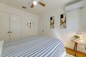 Een slaapkamer met een bed, een plafondventilator, een airconditioning en een nachtkastje met een lamp en een plant.
