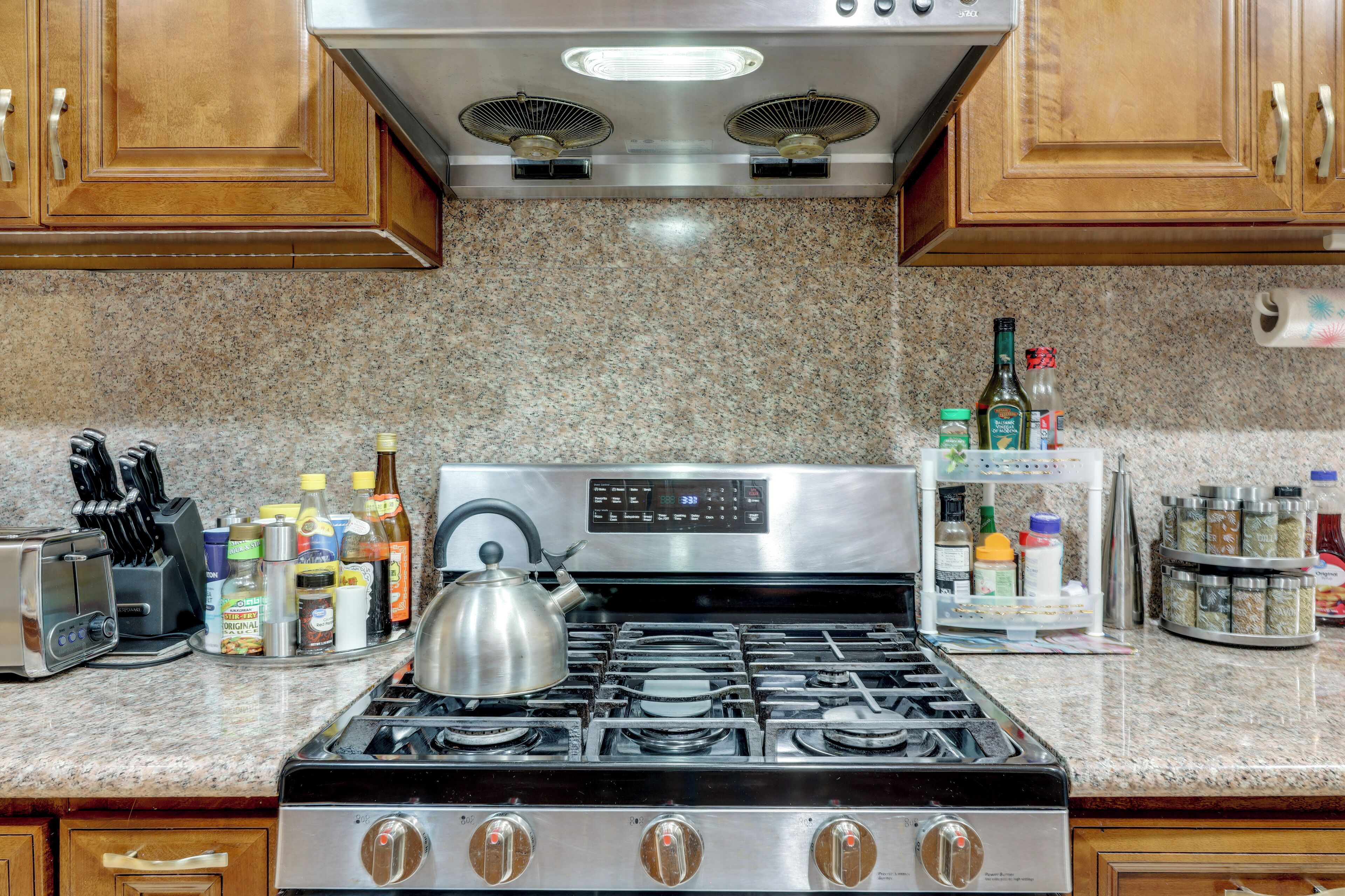 A kitchen with a stove, a kettle, and various kitchen items on the counter.