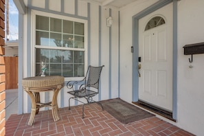 A front porch with a wicker table and chair, a white door with a mailbox, and a brick floor. - 12 Mi to Downtown LA: Central SoCal Base (Rosemead)