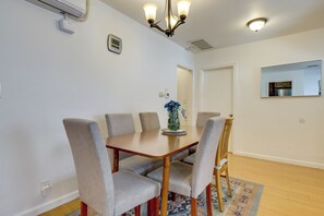 Een eetgedeelte met een houten tafel, vier gestoffeerde stoelen, een vaas met bloemen en een kamerbreed tapijt met een patroon.