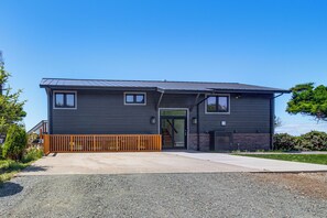 A modern two-story house with a dark exterior, a wooden deck, and a clear sky.