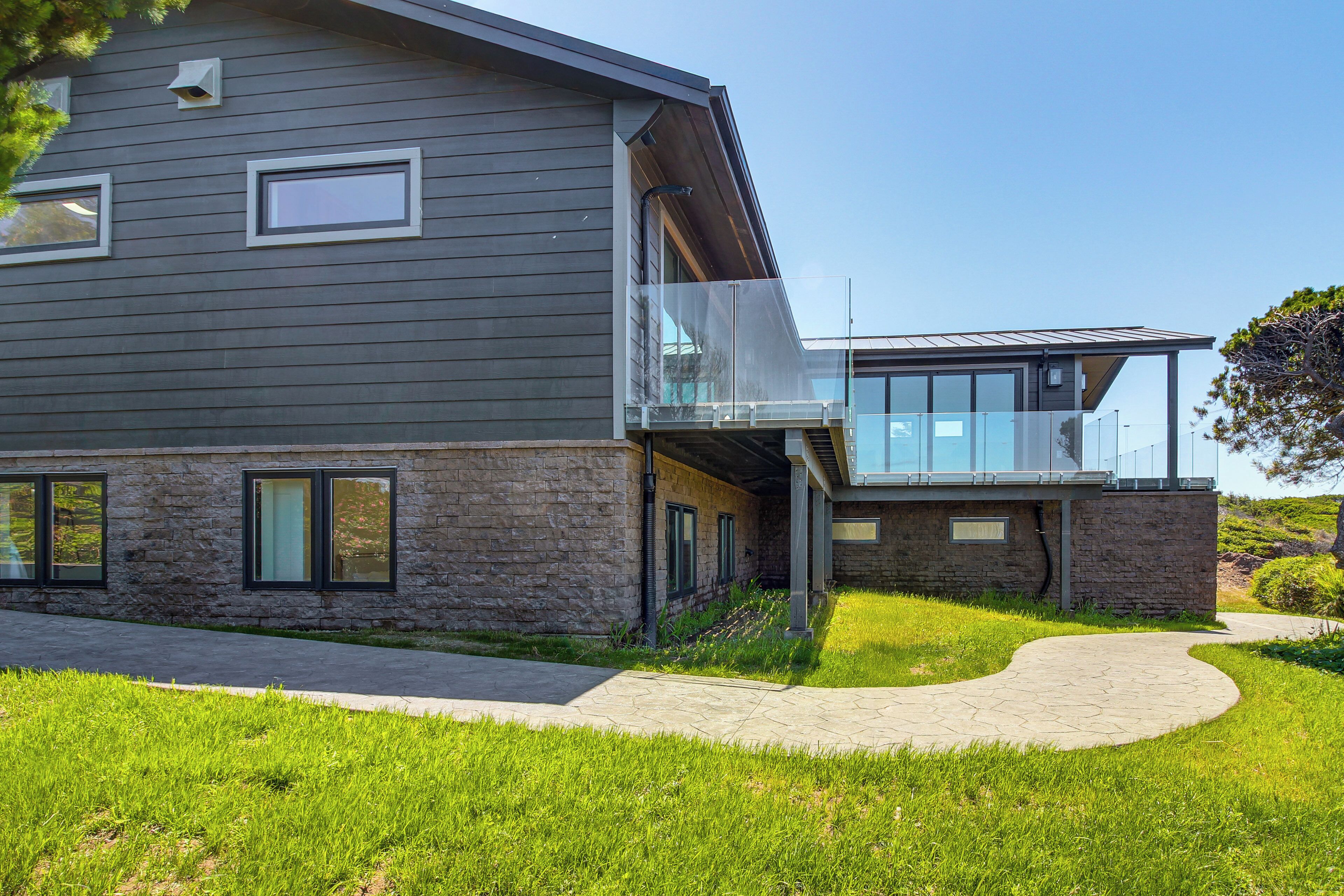 A modern two-story house with a stone facade, large windows, and a covered outdoor area.