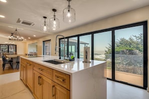 A modern kitchen with a large island, stainless steel appliances, and a view of the ocean.