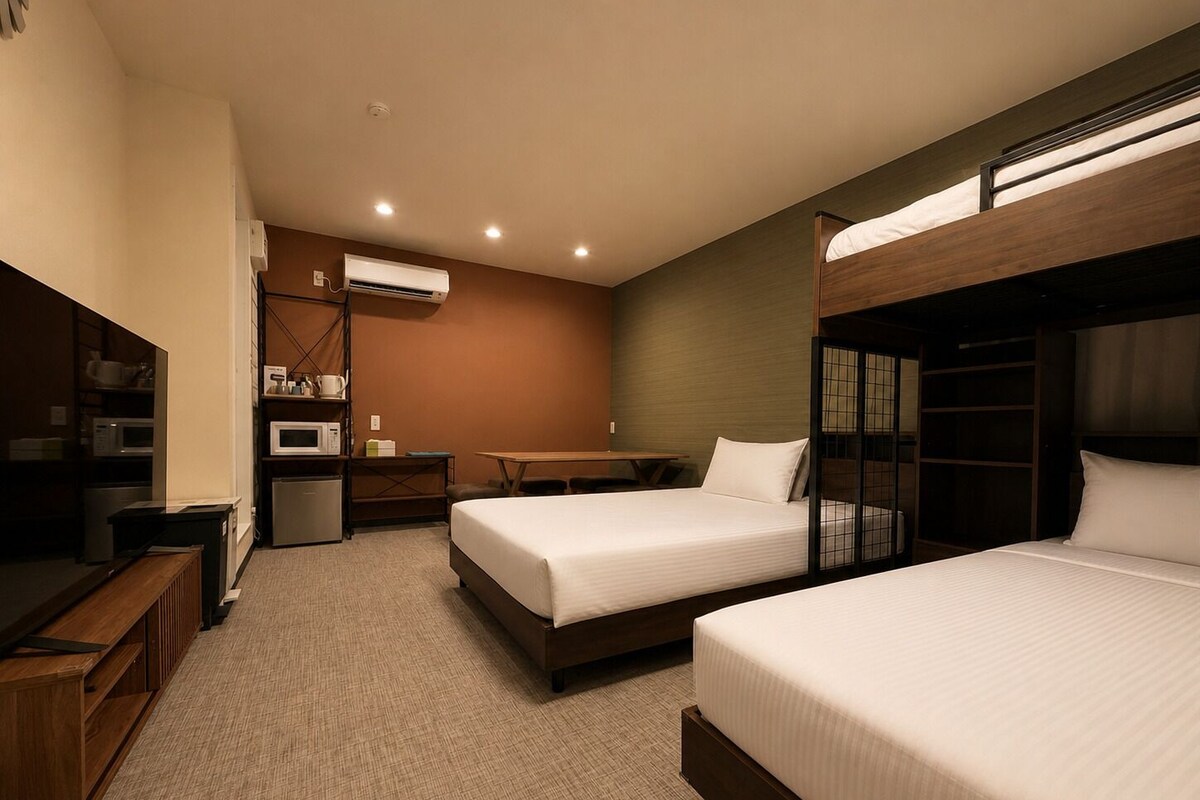 A hotel room with bunk beds, a kitchenette, a desk, and a TV.