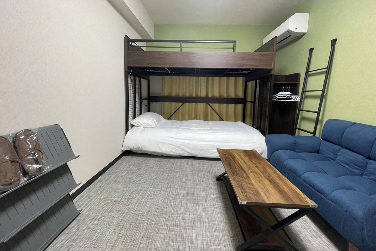 A bunk bed room with a single bed, a blue sofa, a small wooden table, and a radiator.