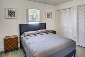Een slaapkamer met een bed, nachtkastjes, een raam en een set witte verstelbare deuren.