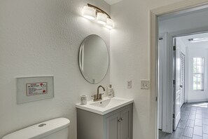 Een badkamer met toilet, wastafel en spiegel. Er hangt een bord aan de muur en een deur leidt naar een andere ruimte.