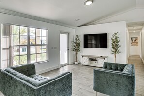 Een moderne woonkamer met twee grijze gestoffeerde fauteuils, een flatscreen-televisie aan de muur en een houten console tafel.