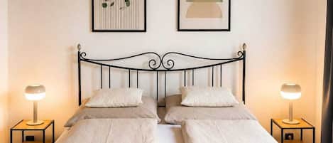 A bed with a black metal frame, two bedside tables with lamps, and two framed artworks on the wall.