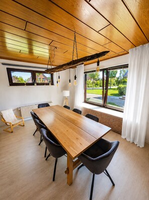 Ein Konferenzraum mit einem Holztisch, schwarzen Stühlen, einem weißen Heizkörper und Blick auf Grünflächen durch große Fenster.