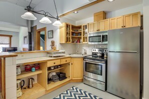 A modern kitchen with wooden cabinets, stainless steel appliances, and a herringbone-patterned rug. - Deck & Wooded Views! 2 Mi to Frederick Gunn School (Washington)